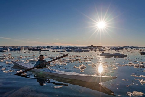 Child paddling in sea kayak through ice floes in the sea, kayak, backlight, sunbeams, summer,