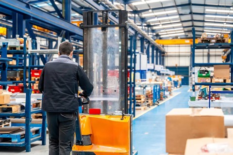 Warehouse worker walking among shelves with handcart in a logistic factory