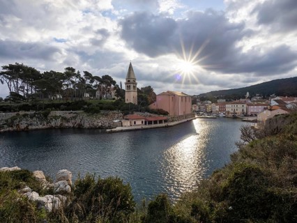 Sun breaking through clouds, view of the harbour entrance of Veli Losinj, with St. Anthony's