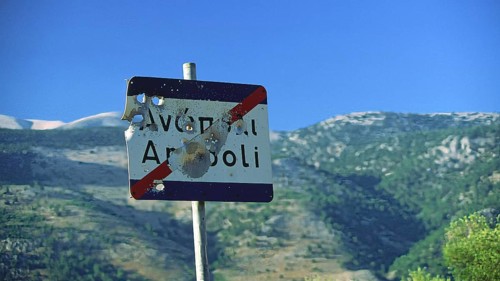 A damaged road sign with bullet holes, in the background a picturesque mountain landscape,