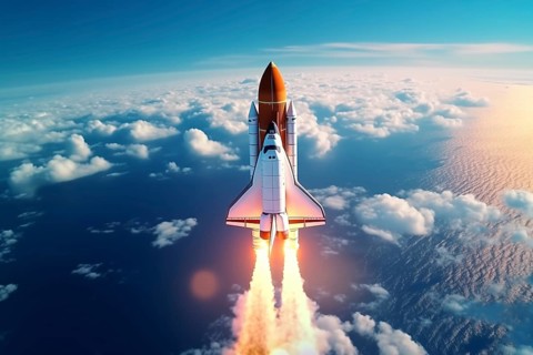 Aerial view of a rocket shuttle carrier launch at sunrise over an ocean coast. The rocket is