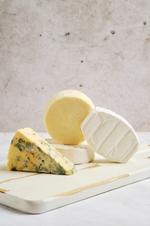 Pieces of brie, camembert, goat cheese and cheese with blue mold on wooden serving board