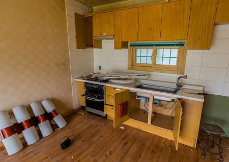 Kitchen area of abandoned house with dirt and electrical fixtures debris on counter top and leaning
