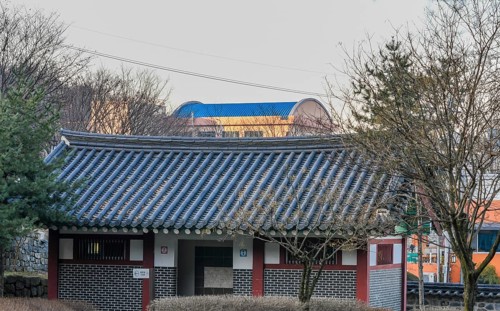 Public restroom in woodland park with a tiled roof surrounded by trees and brushes with a modern