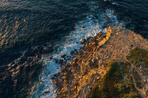 Drone top down view of ocean waves break on rocky headland. Drone shot of sea blue waves beat and