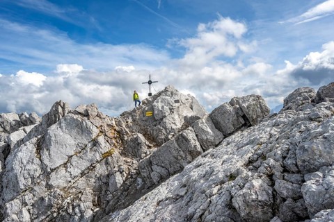 Mountaineer on the rocky summit of the Watzmann Mittelspitze with summit cross, Watzmann crossing,