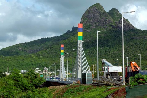 A highway with Mauritian emblem on pillar and a truck driving, surrounded by mountains and an