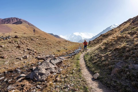 Mountaineer in the Achik Tash valley, behind glaciated and snow-covered mountain peak Pik Lenin,