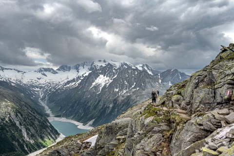 Two mountaineers on hiking trail with snow, view of Schlegeisspeicher, glaciated rocky mountain