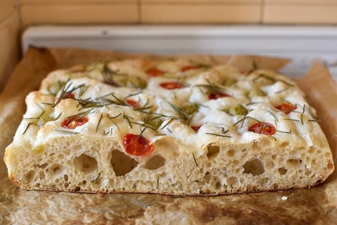 Homemade Italian flatbread focaccia with cherry tomatoes, olives and rosemary in a rustic kitchen
