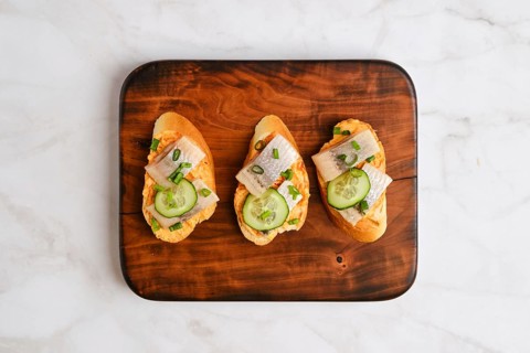 Top view of sandwiches with pieces of Clupeidae and spring onion on wooden serving board