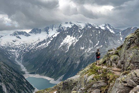 Mountaineer on hiking trail, view of Schlegeisspeicher, glaciated rocky mountain peaks Hoher