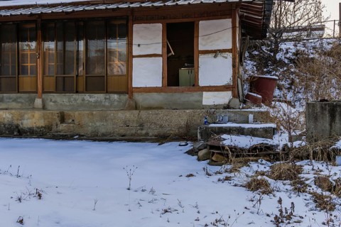 Old abandoned wooden house with sliding doors and concrete porch and snow covered lawn in a rural