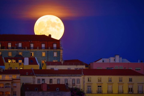 Beautiful view of big full moon rising behind a row of old houses in European city, Lisbon,