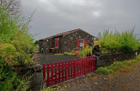 Stone house with red shutters and door and a red fence in a rural area, North Coast, Santa Luzia,