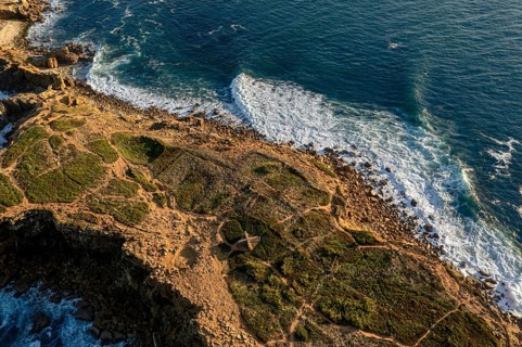 Ocean waves break on rocky island shores at sunset. Drone shot of sea blue waves beat and splash in
