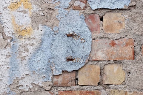 A weathered wall with remains of plaster and exposed bricks, old wall of red bricks with blue,