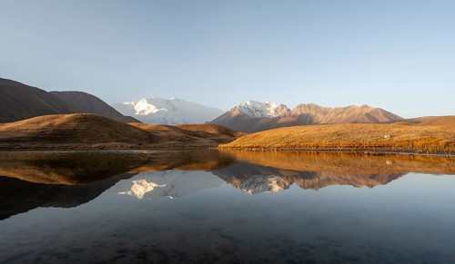 White glaciated and snowy mountain peak Pik Lenin at sunrise, mountains reflected in a lake between