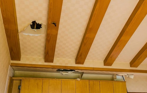 Holes and torn wallpaper in ceiling above kitchen cabinets in abandoned house
