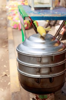 Vertical view of a metal steamer for cooking whole corn cob at the sidewalk, a popular khmer