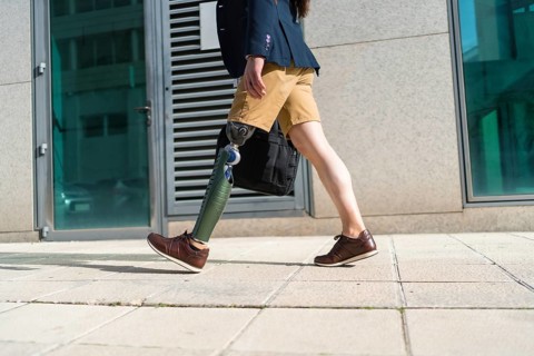 Lower part of an unrecognizable businessman with prosthetic leg walking along a financial district