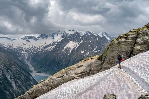 Mountaineer on hiking trail with snow, view of Schlegeisspeicher, glaciated rocky mountain peaks