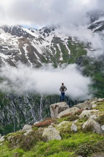 Mountaineer standing on a rock, cloudy mountain landscape with blooming alpine roses, view of rocky