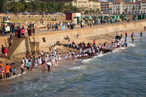 School children paddle in the sea on small sandy beach at Galle Face Green, Colombo, Sri Lanka,