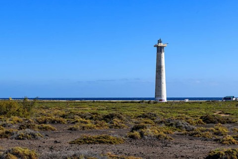 View of lighthouse Faro de Morro Jable on east coast of peninsula Jandia, in the foreground green