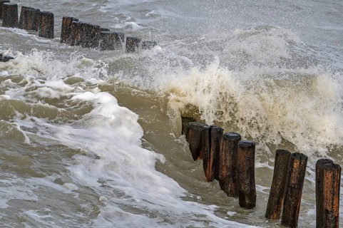 Wave crashing into wooden groyne, breakwater to avoid beach sand erosion during winter storm along
