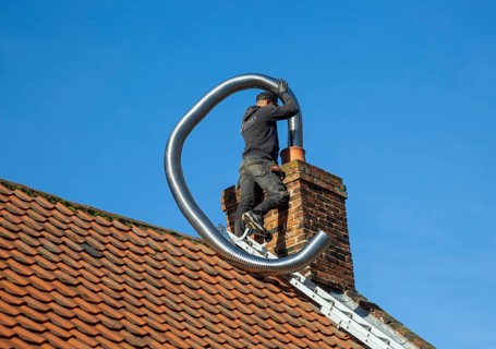 Man fitting chimney liner on roof of home, Shottisham, Suffolk, England, UK
