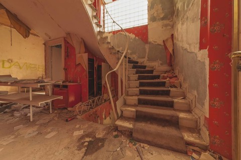 Dilapidated interior staircase of a building with graffiti lettering 'DANGER' on the wall,