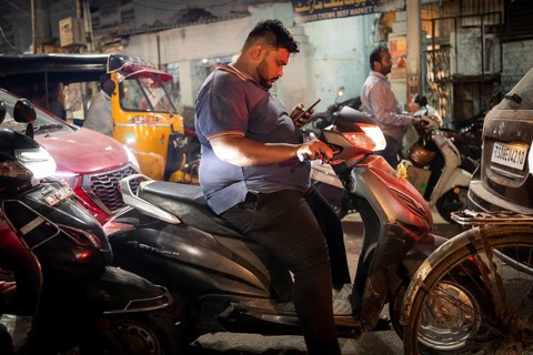 Man on scooter standing in a traffic jam looking at his mobile phone, Hyderabad, Andhra Pradesh,