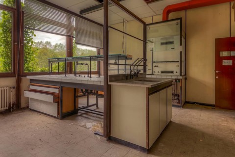 An empty laboratory room with a view of nature through windows, littered with scraps of paper,
