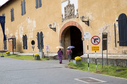 Women walking with umbrellas for shade towards the fort doorway exit in the historic town of Galle,