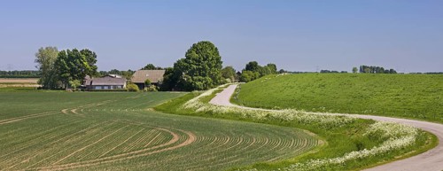 Rural landscape showing winding road, farm with farmland and dyke, dike in spring at