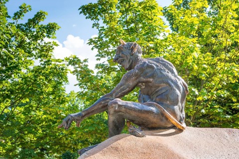 Bronze statue depicting a grinning, laughing naked fantasy figure, placed on a rock, statue,