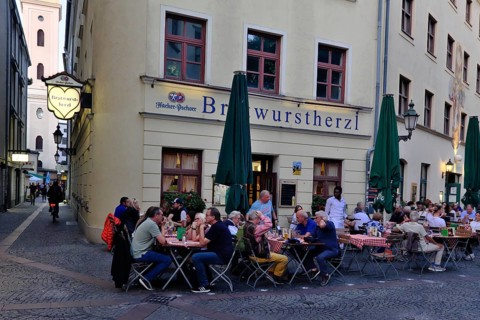 People sitting in the garden in front of the traditional restaurant Bratwurstherzl at