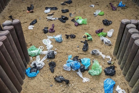 Fenced sandy public dog toilet area in city park filled with colourful discarded plastic dog poop