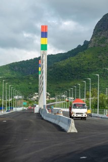 A highway with Mauritian emblem on pillar and a truck driving, surrounded by mountains and an