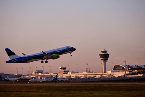 AirBaltic Airbus A220 taking off on Runway South with Terminal 1 and Tower in the sunset, Munich