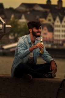 A man sits on the riverbank enjoying a drink in the evening, Hohenzollernbruecke, Cologne Deutz,