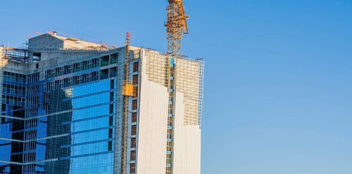 Yellow crane elevator attached to side of building that is under construction against a clear blue