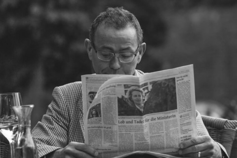 A man engrossed in reading a newspaper at an outdoor table, Wuppertal Elberfeld, North