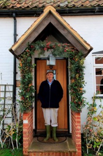 Elderly man standing in his porch having decorated it for Christmas, Suffolk, England, UK