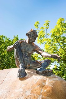 Bronze statue depicting a grinning, laughing naked fantasy figure, placed on a rock, statue,