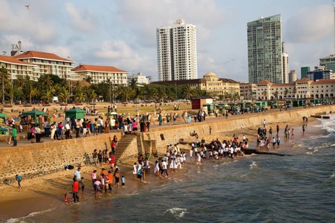 School children paddle in the sea on small sandy beach at Galle Face Green, Colombo, Sri Lanka,