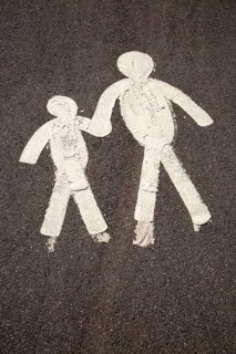 Child and parent figures holding hands on tarmac pavement, Mumbles, South Wales, UK
