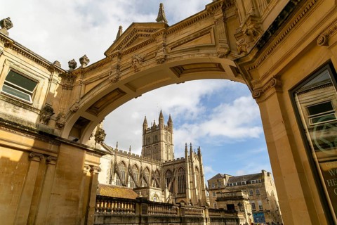 View of abbey church and Roman Baths from under stone archway, York Street, Bath, Somerset,