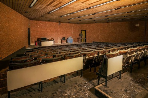 An abandoned lecture theatre with damaged wooden seats and a spherical model on the stage, Biotech,